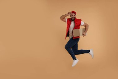 Açık kahverengi arkaplan üzerine paket ile mutlu genç kurye atlama, metin için boşluk