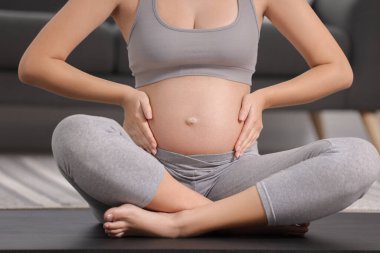 Evde yoga minderinde oturan hamile kadın, yakın plan.