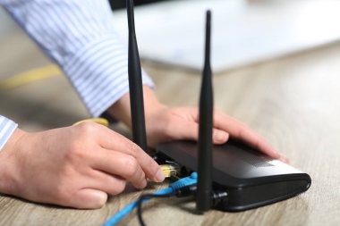 Kadın içerideki masadaki kablosuz internet yönlendiricisine ethernet kablosu yerleştiriyor.