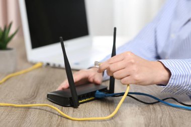 Bir kadın ahşap masadaki kablosuz internet yönlendiricisine ethernet kablosu yerleştiriyor.