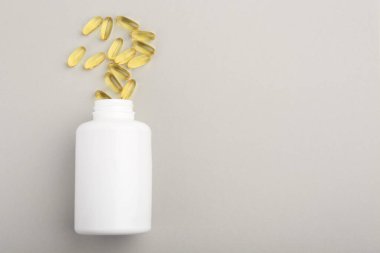 Açık gri arka planda şişe ve vitamin kapsülleri, üst manzara. Metin için boşluk