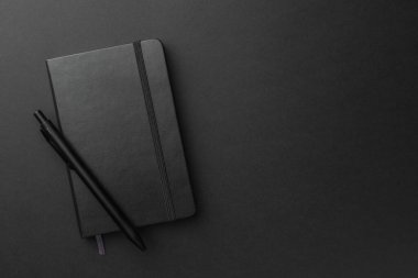 Siyah arka planda kapalı defter ve kalem, üst görünüm. Metin için boşluk