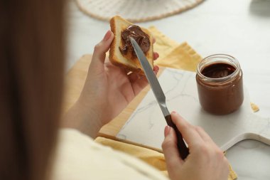 Beyaz masadaki tostun üzerine fıstık ezmesi döken bir kadın.