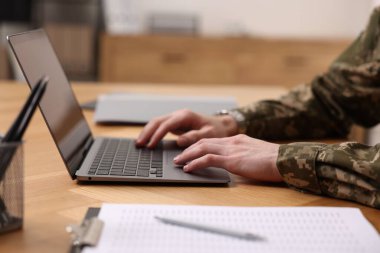 Askerlik. Asker bilgisayarla çalışıyor, ahşap masada, yakın plan.