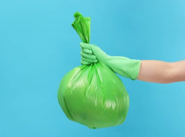 Açık mavi arka planda çöp dolu plastik poşet taşıyan bir kadın, yakın plan. Metin için boşluk