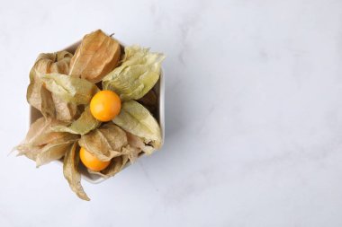 Beyaz mermer masadaki kalixli olgun physalis meyveleri, üst manzara. Metin için boşluk