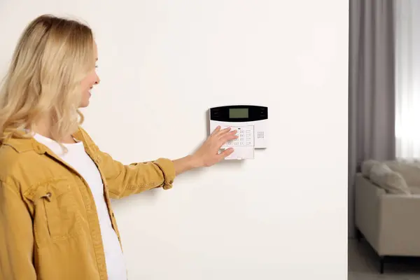 Woman entering code on home security system indoors