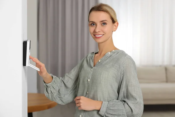 Smiling woman entering code on home security system in room