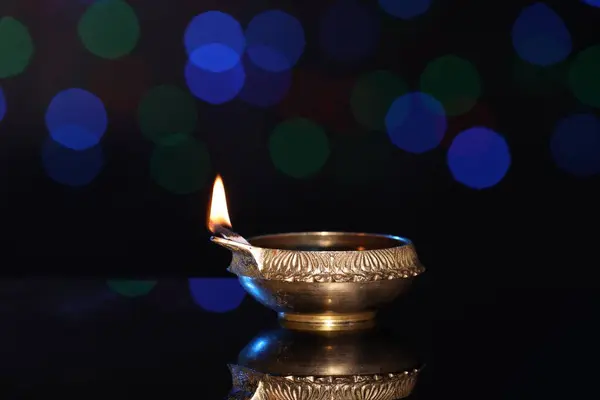 stock image Lit diya on dark background with blurred lights, space for text. Diwali lamp