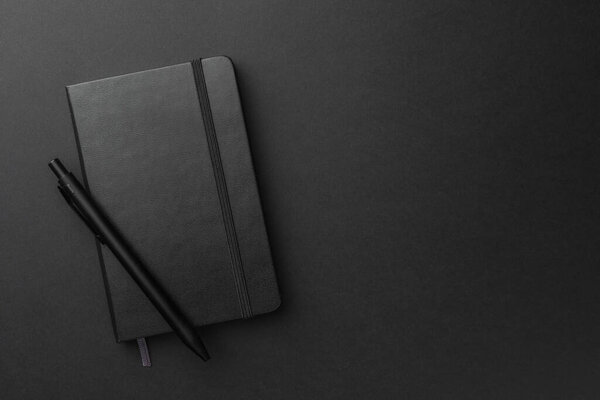Closed notebook and pen on black background, top view. Space for text