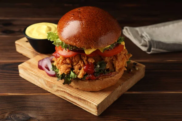 Delicious burger with crispy chicken patty and sauce on wooden table