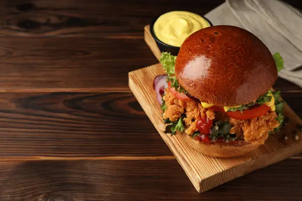 Delicious burger with crispy chicken patty and sauce on wooden table. Space for text