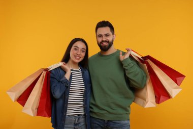 Turuncu arka planda alışveriş torbaları olan mutlu bir çift.