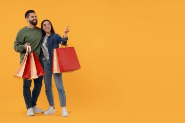 Alışveriş torbalı mutlu çift turuncu arka planda bir şeye bakıyor. Metin için boşluk