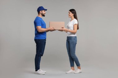 Gülümseyen kurye gri arkaplandaki alıcıya paket veriyor
