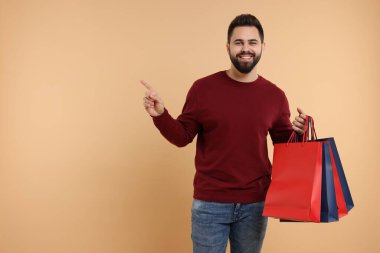 Elinde bir sürü kese kağıdıyla gülümseyen adam bej arka plandaki bir şeyi işaret ediyor. Metin için boşluk