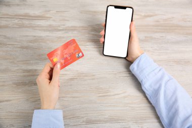 Çevrimiçi ödeme. Kredi kartı ve akıllı telefon kullanan bir kadın. Açık tahta masada boş ekranlı, üst görüşlü.