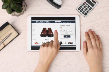 Tabletli bir kadın beyaz ahşap masada internetten alışveriş yapıyor.