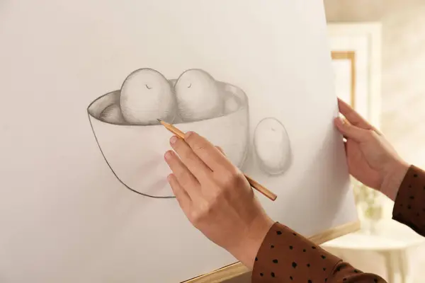 Woman drawing bowl of fruits with graphite pencil on canvas indoors, closeup
