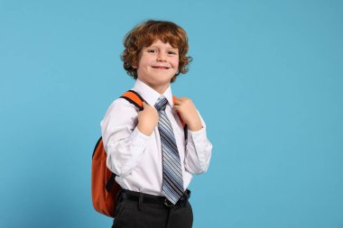 Açık mavi arka planda sırt çantalı mutlu okul çocuğu.