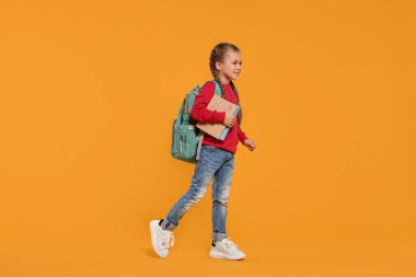Sırt çantası ve turuncu arka plan kitapları olan mutlu bir kız öğrenci.