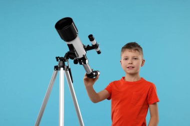 Açık mavi arka planda teleskopu olan sevimli küçük bir çocuk.