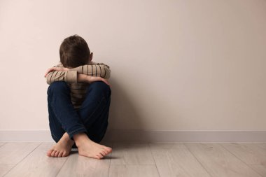 Çocuk istismarı. Kapalı alanda bej duvarın yanında oturan üzgün çocuk, mesaj için yer var.