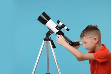 Küçük çocuk teleskopla açık mavi arkaplanda yıldızlara bakıyor.