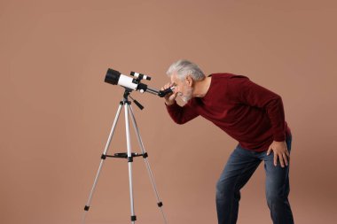 Kıdemli astronom yıldızlara kahverengi arkaplanda teleskopla bakıyor.