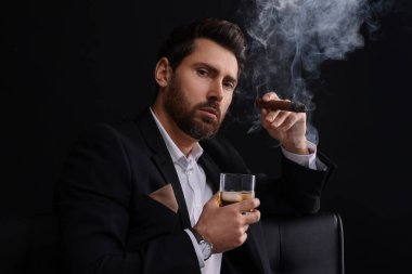 Siyah arka planda puro içen zarif takım elbiseli yakışıklı bir adam.