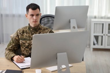 Military service. Young soldier working at wooden table in office clipart