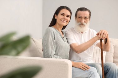 Bastonlu yaşlı bir adam ve kanepede oturan genç bir kadın.