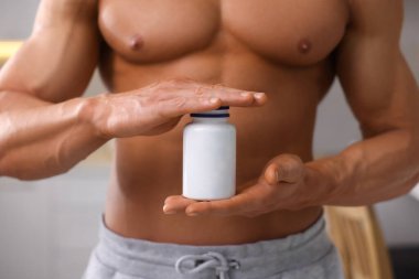 Kapalı alanda bir şişe takviyeli atletik adam, yakın plan. Kilo kaybı