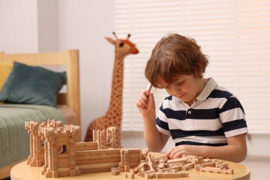 Odadaki ahşap inşaat setiyle oynayan sevimli küçük çocuk. Çocuk oyuncağı