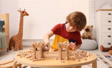 Küçük çocuk masadaki ahşap giriş kapısıyla oynuyor. Çocuk oyuncağı