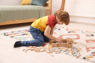 Odadaki halının üzerinde ahşap inşaat setiyle oynayan küçük bir çocuk. Çocuk oyuncağı