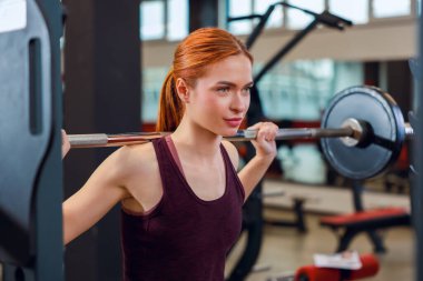 Spor salonunda halter eğitimi almış atletik bir genç kadın.