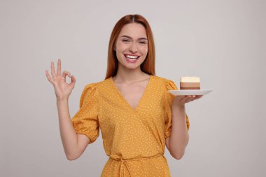 Lezzetli pastası olan genç bir kadın açık gri arka planda iyi bir jest gösteriyor.