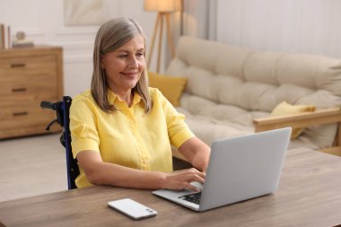Tekerlekli sandalyedeki kadın ofisteki masada dizüstü bilgisayar kullanıyor.