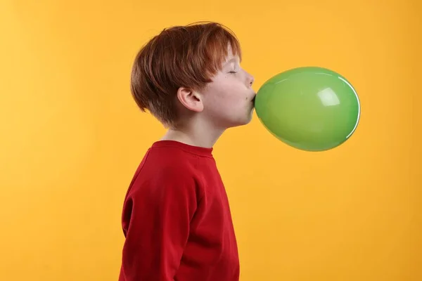 Boy inflating green balloon on orange background