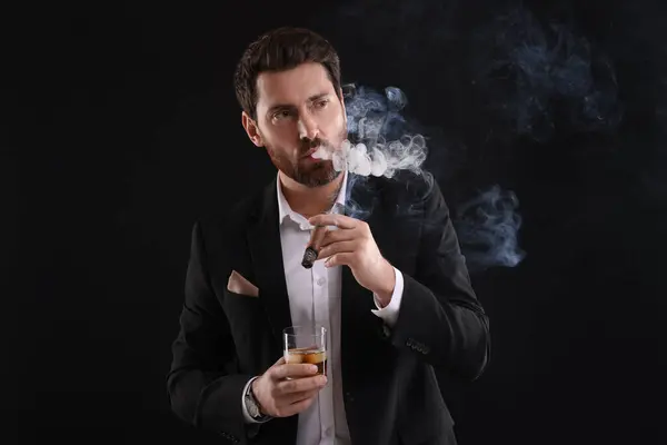 黒い背景にウイスキーを吸うタバコのガラスとエレガントなスーツのハンサム男 — ストック写真