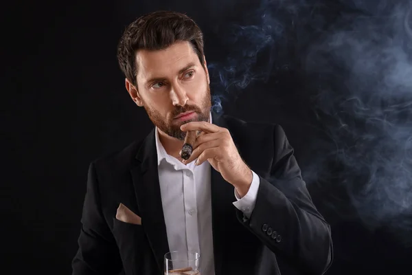 黒い背景にウイスキーを吸うタバコのガラスとエレガントなスーツのハンサム男 — ストック写真