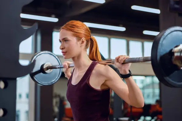 Athletic young woman with barbell training in gym