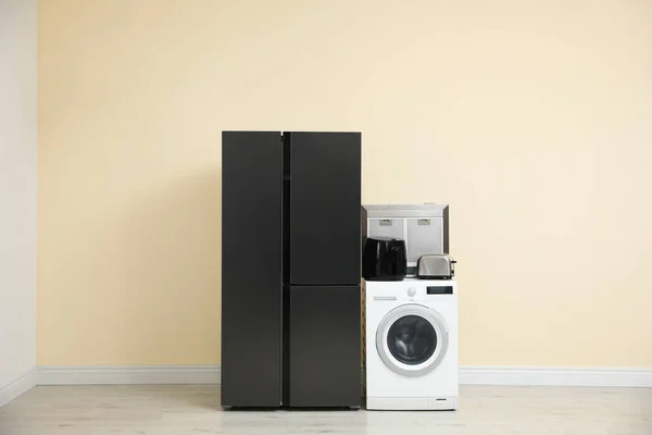 Modern refrigerator and other household appliances near beige wall indoors
