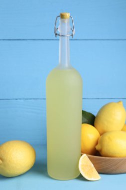 Bir şişe lezzetli limoncello likörü ve açık mavi masada limonlar.