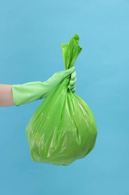 Açık mavi arka planda çöp dolu plastik poşet taşıyan kadın, yakın plan.