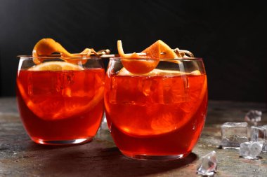 Aperol sprey kokteyli, buz küpleri ve portakal dilimleri gri desenli masada, yakın plan.