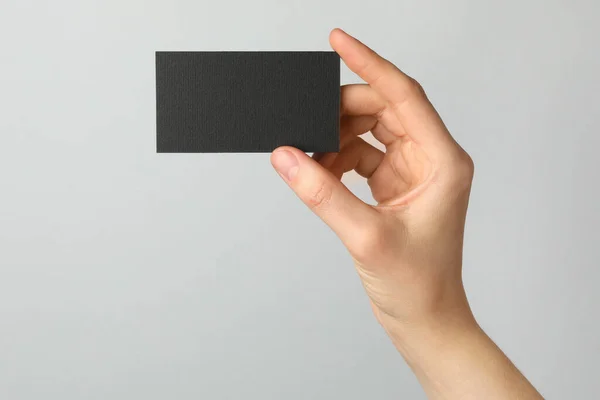 Woman with blank black business card on light grey background, closeup. Mockup for design