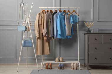 Gri duvarın yanında değişik şık kadın kıyafetleri, ayakkabıları ve çantaları var.