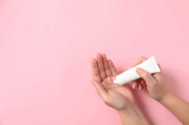 Kadının biri pembe arka planda eline tüpten kozmetik krem sürüyor. Metin için boşluk